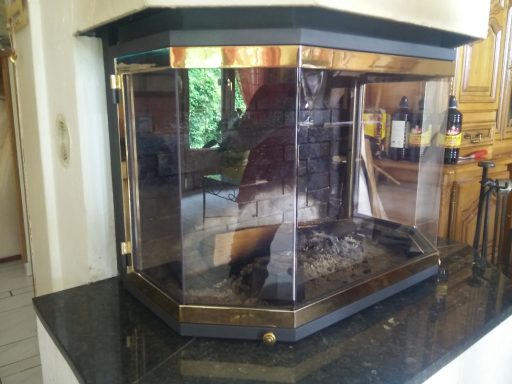 Cheminée moderne en verre sur un meuble en pierre noire, entourée de lumière naturelle.