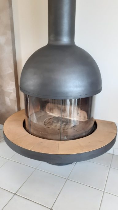 Poêle à bois moderne avec une base en bois, son design arrondi et cheminée verticale.