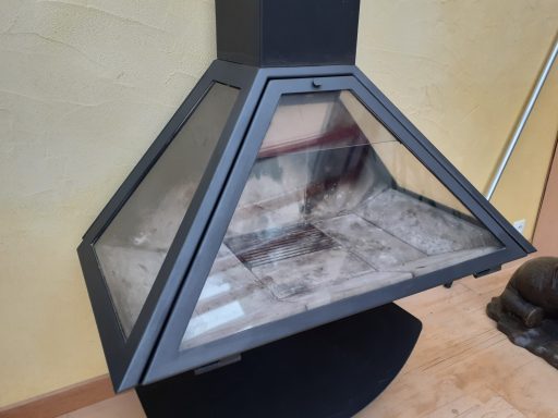 Cheminée moderne en métal noir avec un vitrage sur trois côtés, montée sur un socle.